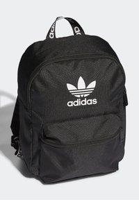 Svart tygryggsäck med rundad form, med en stor framficka och vitt Adidas-logga. Justerbara remmar och bärhandtag ingår.