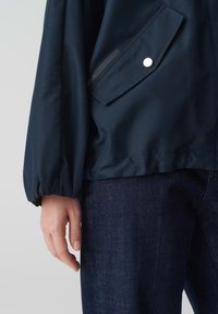 Marineblauwe jas met een kort ontwerp, elastische boorden en een klepzak. Voorzien van glad, waterbestendig stof en een gestroomlijnd silhouet.