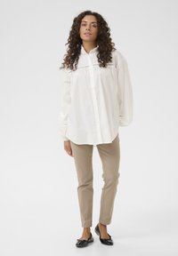 White button-up shirt with puffed sleeves, soft fabric, and subtle detailing; paired with beige slim-fit pants and black ballet flats.