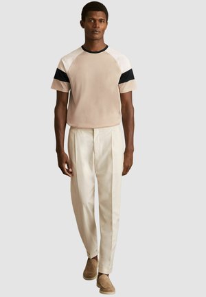 Beige t-shirt med kort ärm och svarta samt vita detaljer, kombinerad med skräddarsydda krämfärgade byxor och bruna skor, med en avslappnad passform.