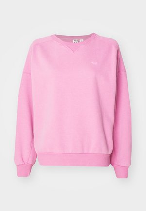 Ružová mikina vyrobená z mäkkej, štruktúrovanej tkaniny. Má výstrih do V, spustené ramená a rebrované manžety a lem. Na hrudi je jemný detail loga.