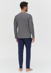 Męski zestaw piżamowy składający się z długiego rękawa topu w czarno-białą kratkę oraz jednolitych granatowych spodni, wykonany z miękkiej dzianiny bawełnianej.