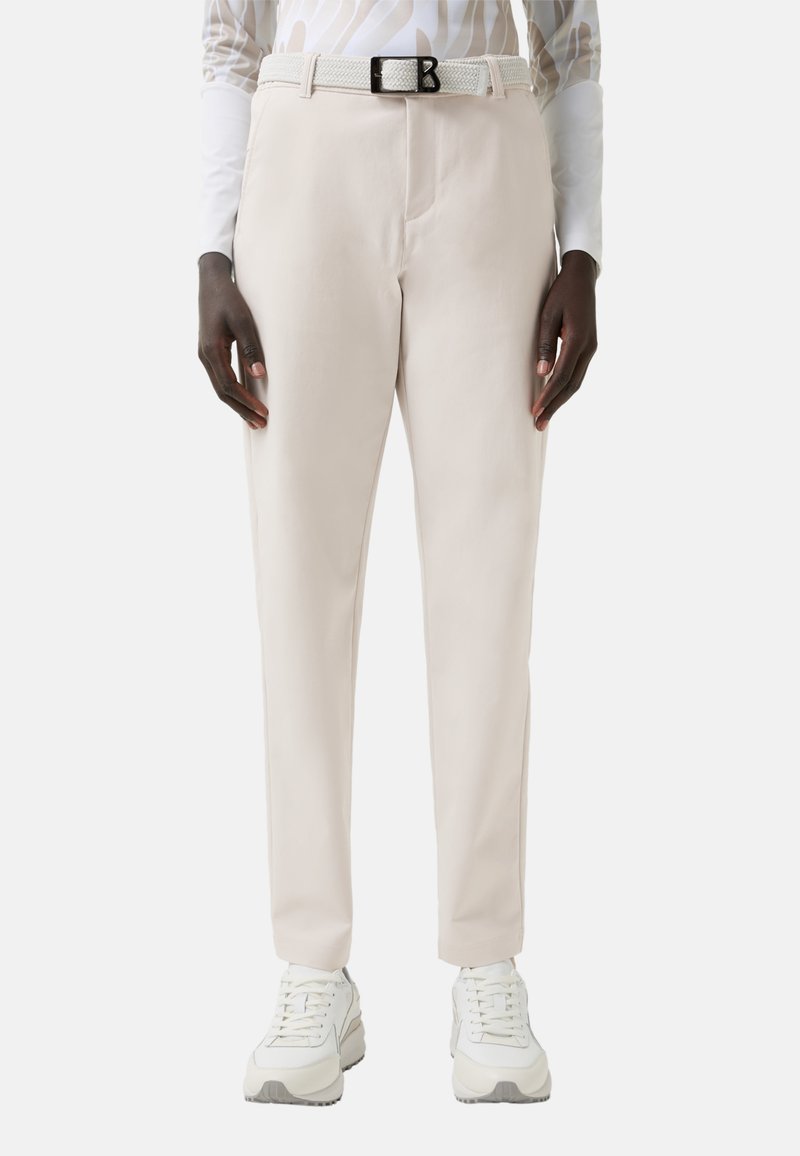 Světlé béžové kalhoty na míru s hladkou texturou, vybavené bílým tkaným pásem a černou sponou, doplněné bílými teniskami.