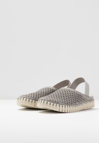 Scarpe grigie slip-on con retro aperto, dotate di una tomaia testurizzata e perforata e una suola bianca dentellata. Fascetta elastica per una vestibilità sicura.