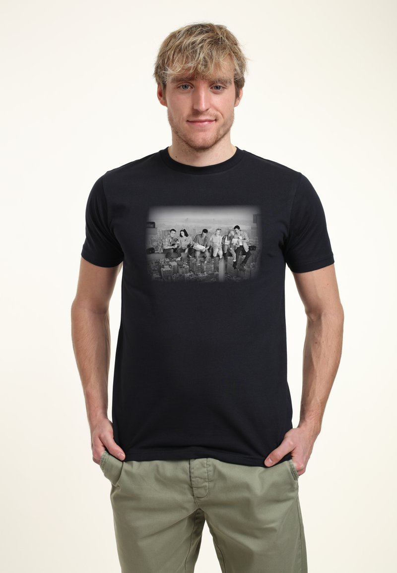 Svart bomull T-shirt med ett monokromt fototryck av fem personer som sitter på en balk, med en stadssilhuett i bakgrunden.