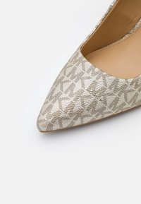 Chaussure plate pointe pointue avec motif texturé beige et brun clair et logo "Michael Kors" sur le dessus.