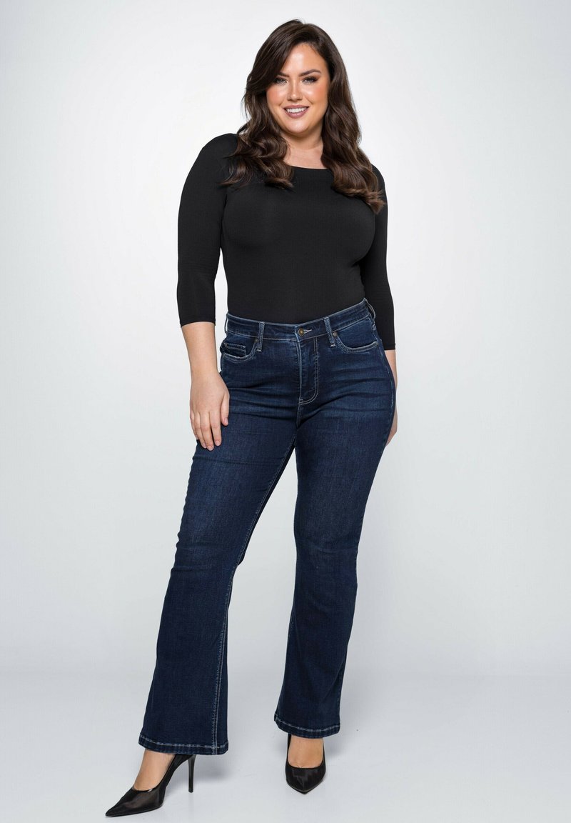 Zwarte lange mouwen bodysuit gecombineerd met donkerblauwe flared jeans. De jeans hebben voorzakken en een nette, gestructureerde denimafwerking. Zwarte hoge hakken.