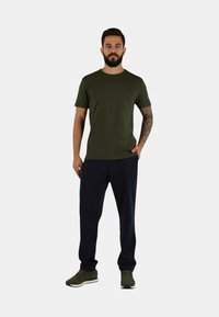 Maglietta verde oliva a maniche corte, abbinata a pantaloni della tuta blu navy e scarpe da ginnastica verdi. Presenta un design semplice senza motivi.