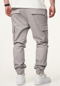 Helle graue Cargo-Hosen mit elastischen Bündchen, seitlichen und hinteren Taschen, aus einem glatten Stoff. Kombiniert mit weißen Sneakern.