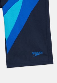 Σκούρο μπλε μαγιό σορτς με διαγώνια διακοσμητικά σε ανοιχτό μπλε και τιρκουάζ χρώμα. Διαθέτει λογότυπο Speedo σε μπλε χρώμα στην κάτω αριστερή ραφή. Ομαλή υφή υφάσματος.