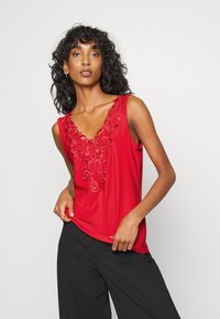 Top sem mangas vermelho com um decote em V profundo, apresentando bordados florais intrincados na gola. Tecido suave com um corte relaxado.