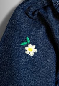 Tumesinises toonis teksariie, millel on väike valge tikitud lill ja rohelised lehed, sile tekstuur ja tihe lõngakoes.