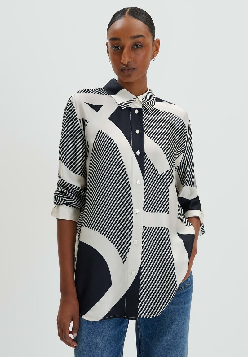 Black and white printed shirt with geometric patterns, button-up front, and rolled sleeves, made of smooth fabric.