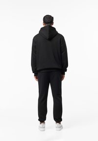 Zwarte hoodie met trekkoord en losse pasvorm, gecombineerd met bijpassende zwarte joggers en witte sneakers. Soepele textuur, minimalistisch ontwerp.