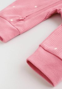Närbild på rosa ribbade babybyxor med små vita prickar och ankelslut på vit bakgrund.