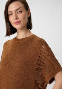 Brauner Strickpullover mit kurzen Ärmeln und einem strukturierten, offenen Strickmuster an den Seiten sowie einem schlichten Rundhalsausschnitt.