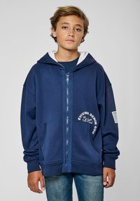 Hoodie zippé bleu marine avec une capuche intérieure blanche, des poches avant et du texte imprimé. Fabriqué en matériau doux avec des poignets et un ourlet côtelés.