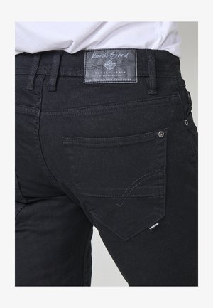 Zwarte denim jeans hebben een gestructureerd oppervlak, een rechte snit en een label op de taille. Bevat twee achterzakken met stikdetails.