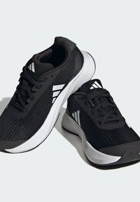 Scarpe da ginnastica nere con una tomaia in mesh testurizzato, dettagli bianchi, design con lacci e una suola sagomata e imbottita per il supporto.