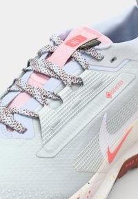 Jasnoniebieskie buty do biegania z teksturowaną cholewką, różowymi akcentami, brązowymi sznurówkami z cętkami oraz metką GORE-TEX zapewniającą odporność na warunki atmosferyczne.