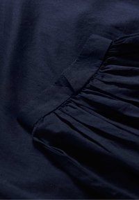 Tecido de algodão azul marinho com detalhe franzido ao longo da borda, textura suave e ligeiro brilho, disposto em uma disposição plana.