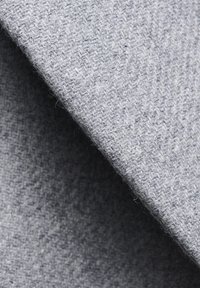 Szary, teksturowany materiał o miękkiej, puszystej powierzchni, przedstawiający wzór tkany. Materiał swobodnie opada, ukazując delikatnie różniące się odcienie szarości.