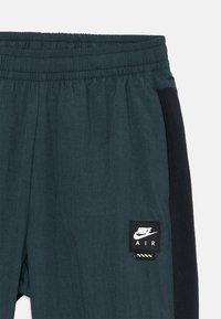 Herr joggerbyxor i mörk teal med elastisk midja, med en svart sidopanel och en rektangulär Nike Air-logotyp.