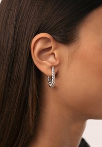 Söljörhängena i silver med en tvinnad design, som har en texturerad yta och en polerad sektion, visas på en modells öra.