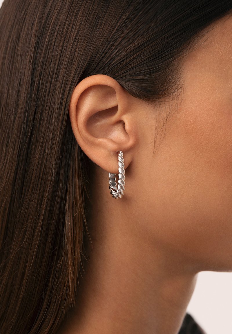 Söljörhängena i silver med en tvinnad design, som har en texturerad yta och en polerad sektion, visas på en modells öra.