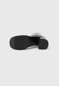 Suola di scarpa nera con tacco, dalla finitura liscia, caratterizzata da una texture gommoso, un tacco arrotondato e una leggera curva sulla punta.