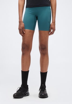 Vihertävänsiniset urheilushortsit joustavasta kankaasta, istuvalla mallilla ja polven yläpuolelle ulottuvalla pituudella. Yhdistetty mustiin sukkiin ja lenkkareihin.