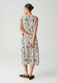 Sleeveless dress in cream with black wave-patterned design, featuring a gathered hem and paired with black mesh shoes.
