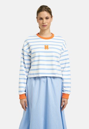 Woman wearing a white and light blue striped sweater with orange collar and cuffs, paired with a light blue striped skirt.