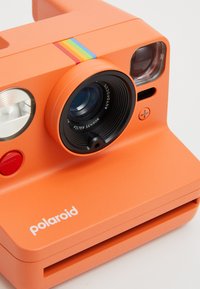 Élénk narancssárga Polaroid azonnali fényképezőgép, téglalap alakú, lencsével, vakuval, színes csíkkal és piros zárgombbal.