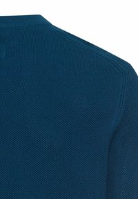 Zbliżenie na teksturowany, granatowy sweter dzianinowy, pokazujący szczegóły szwów na ramieniu i kołnierzu na białym tle.