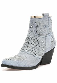 Stivaletto in denim con borchie argentate, punta affusolata e tacco curvo. Presenta cuciture intricate e una finitura testurizzata in azzurro chiaro.