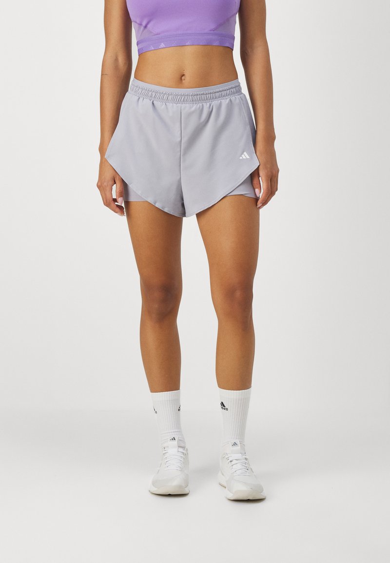 Pantalones cortos activos de color gris claro con un diseño dividido, cintura elástica y acentos de logo en blanco. Combinados con calcetines deportivos blancos y zapatos.