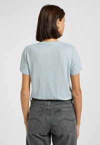 T-shirt azzurro chiaro a maniche corte in un tessuto morbido e testurizzato, abbinato a jeans grigi scuri a vita alta con un design classico delle tasche.