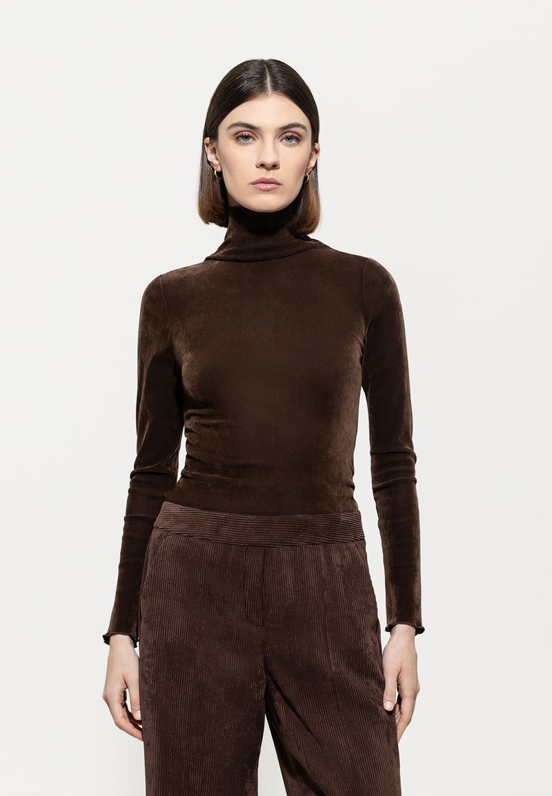 Brown, long-sleeve turtleneck top made of soft material, featuring a fitted design. Paired with textured brown corduroy pants.