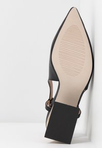 Chaussure noire à bout pointu avec talon bloc, montrant une semelle beige texturée avec des lignes d'adhérence et le texte « Fabriqué en Chine », taille 41.