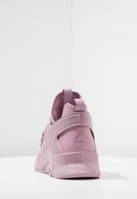 Rosa träningssko med en elegant design, som har ett texturerat tygöverdel, en förstärkt häl och en formad logodetalj.