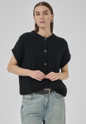 Black short-sleeve cardigan with textured material, five buttons, and a round neckline, paired with light blue high-waisted jeans and a black belt.