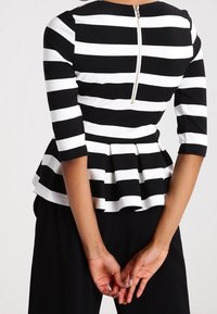 Top péplum avec des rayures horizontales noir et blanc, des manches trois-quarts, un col rond et une fermeture éclair au dos.