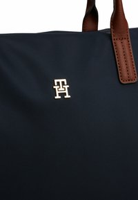 Borsa a spalla in nylon blu navy con manici in pelle marrone e dettaglio del logo dorato, presenta una superficie testurizzata e una forma strutturata.