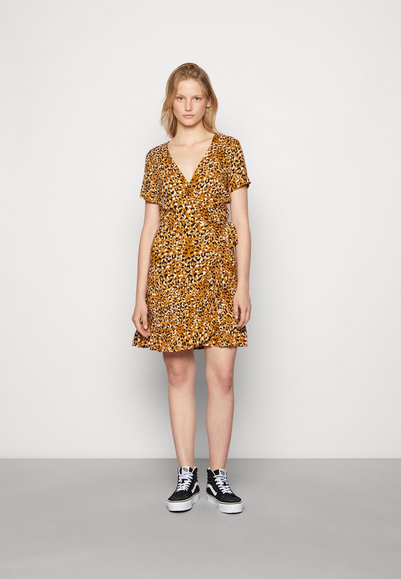 Vestido envolvente em estampado de leopardo laranja e preto, mangas curtas, decote em V, com barra com babados, combinado com sapatilhas altas pretas.