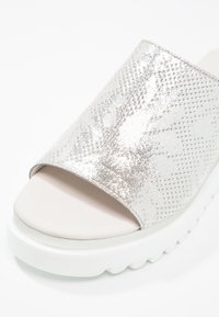Sandale plateforme blanche avec une large bride argentée brillante texturée et une semelle striée.