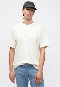 Hele beež värviga soonikkoes t-särk, lõdva lõikega, lühikeste varrukatega ja ümar kaelusega, kantud siniste teksapükstega. Hall nokamüts tikitud detailidega.