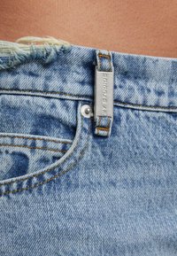 Sinisest toonist denim lühikesed püksid, kulunud äärega ja nähtava õmblusega. Omab metallist tarvikut, millel on graveeritud "2Y Studios".