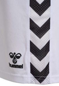 Vit tyg med svart zigzag-mönster och svart Hummel-biklott nära nederkanten, som visar nätstruktur på randen.