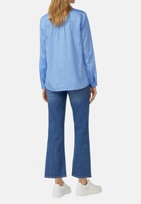 Camicia azzurro chiaro a maniche lunghe con polsini abbottonati, abbinata a jeans a zampa d'elefante blu scuro e sneakers con suola piatta bianche.